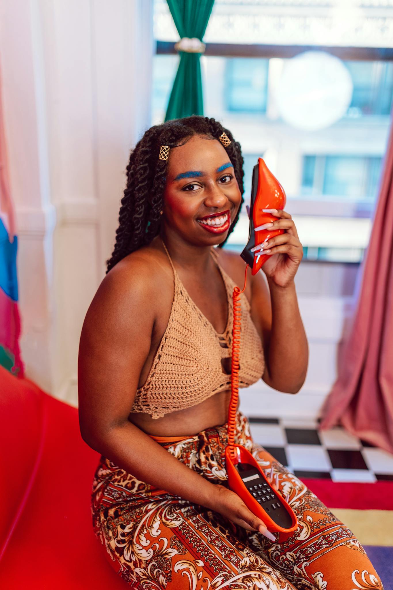 A joyful young woman with colorful makeup holds a retro red phone indoors. Bright and stylish.