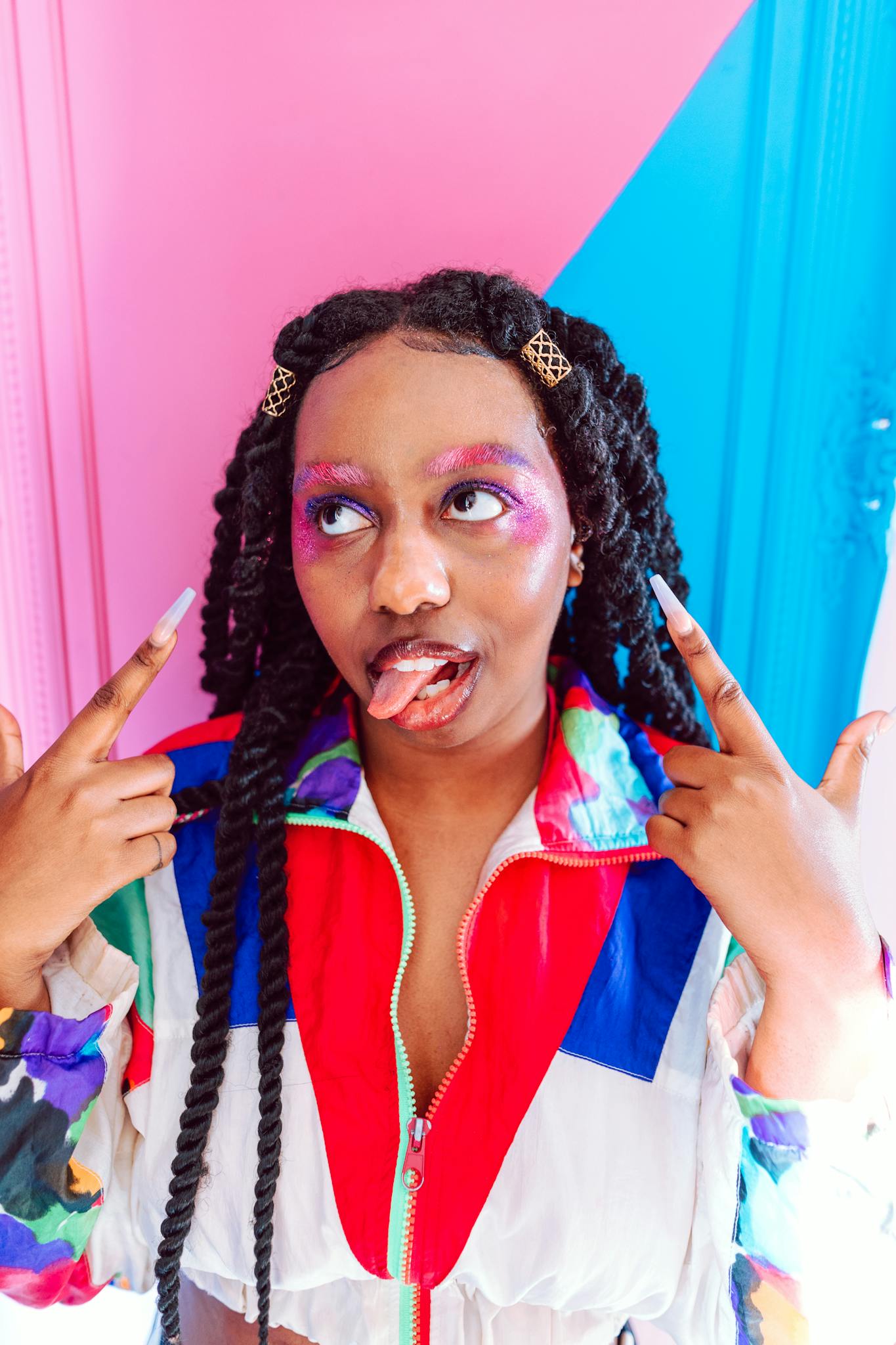 A vibrant portrait of a young woman showcasing colorful makeup and playful fashion indoors.