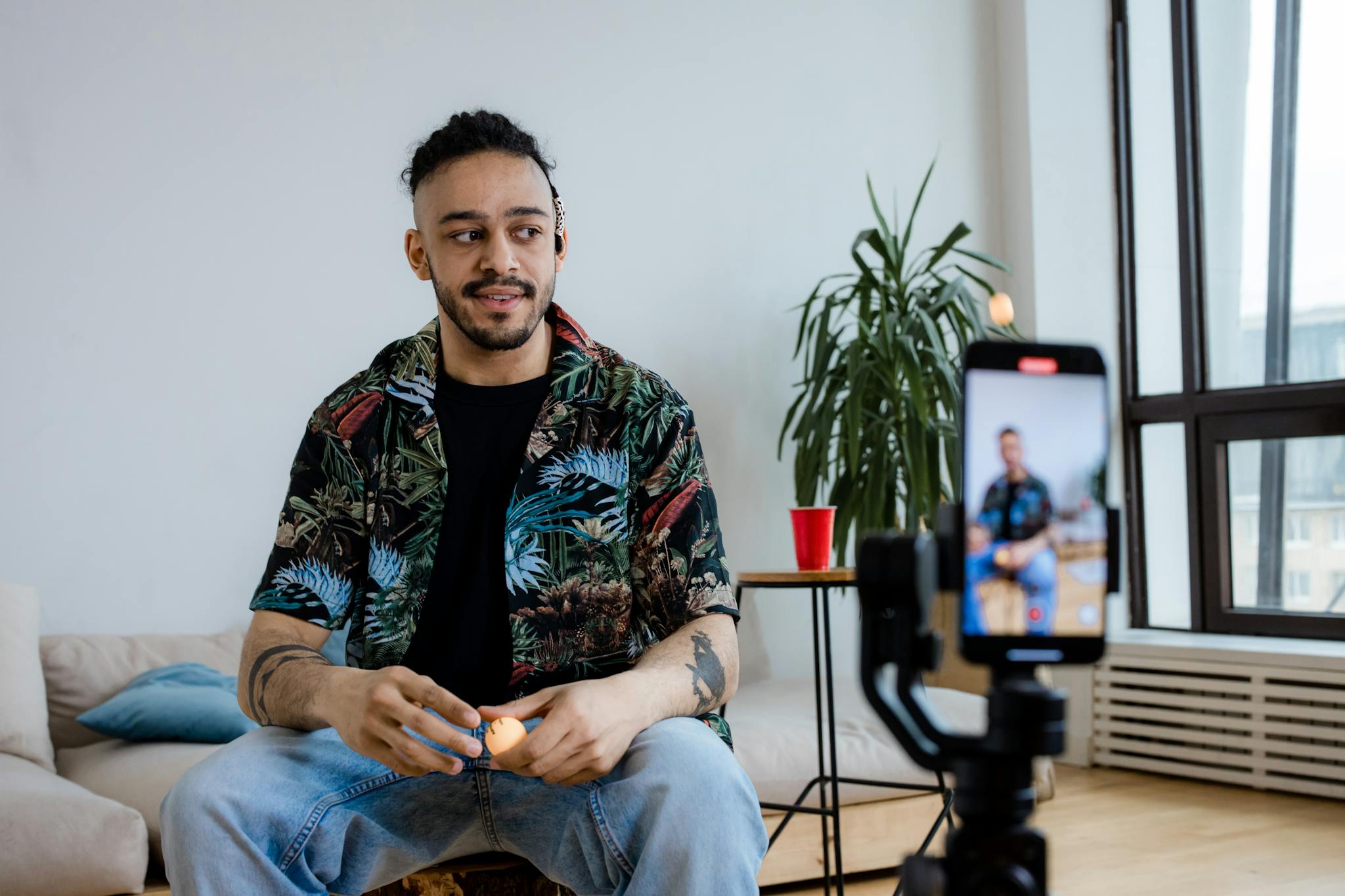 A young man recording video content indoors with a smartphone and tripod.