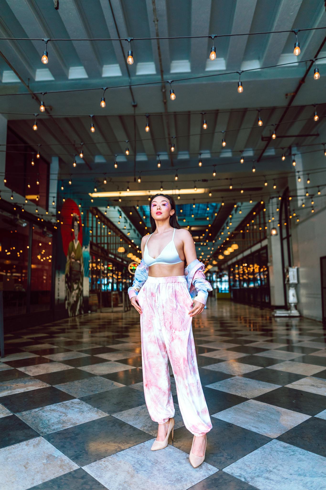 Stylish woman in trendy outfit standing confidently indoors with hanging lights.